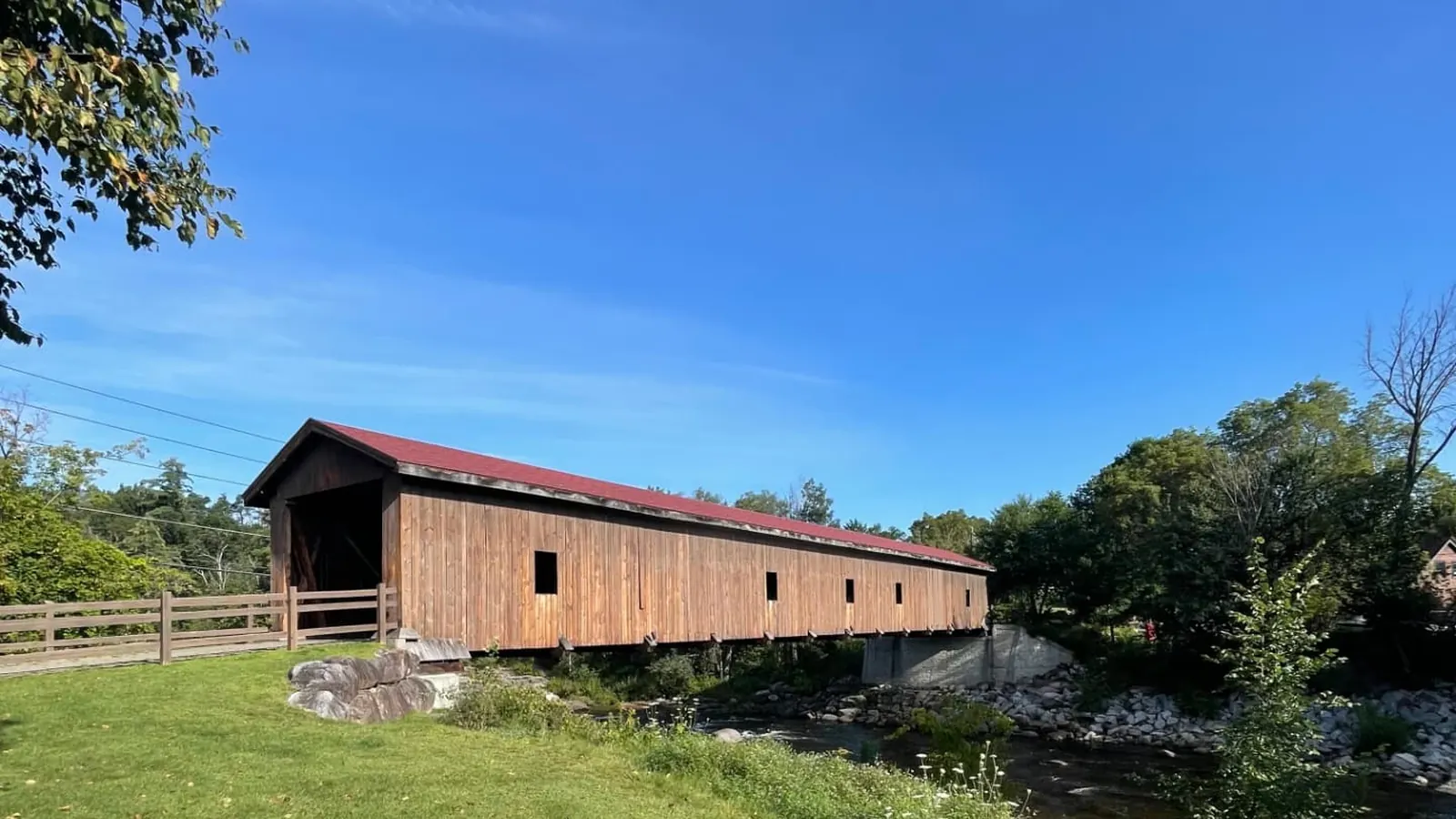 The Jay covered bridge seen across the mown green of the village common, with the river running past its stone abutment