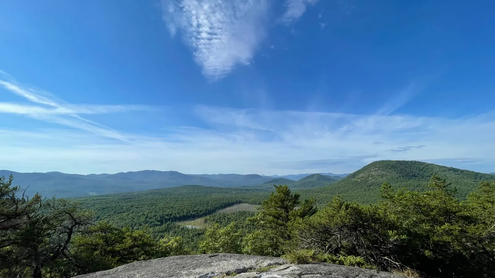 The view from a rock summit above Jay, looking across unbroken forest to ridgelines of Adirondack mountains fading into the distance